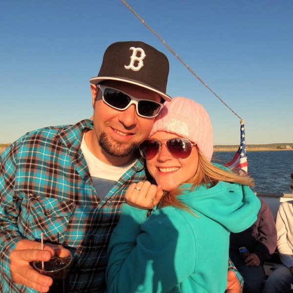a man wearing a hat and sunglasses posing near a body of water