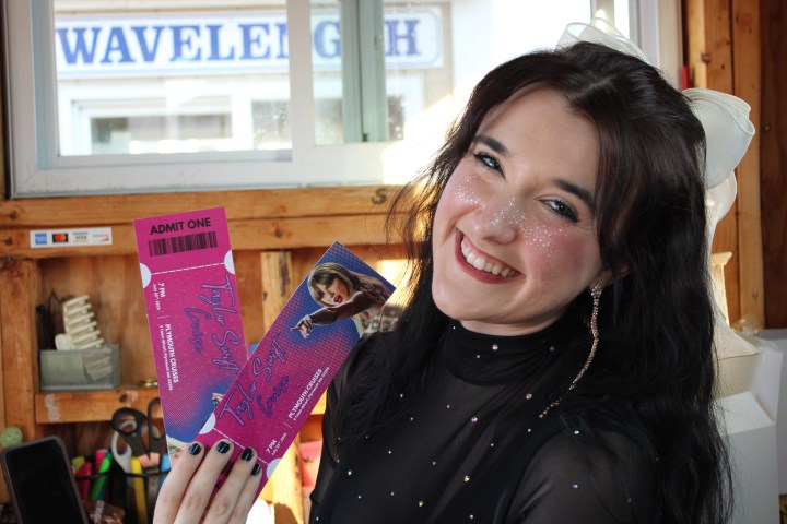 Smiling person with glitter makeup holding two Taylor Swift concert tickets.