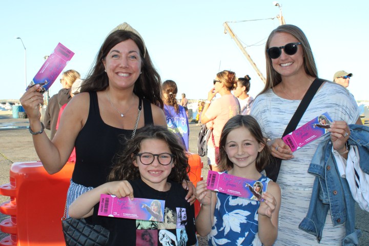 Two women and two girls smiling and holding pink event tickets in an outdoor setting.