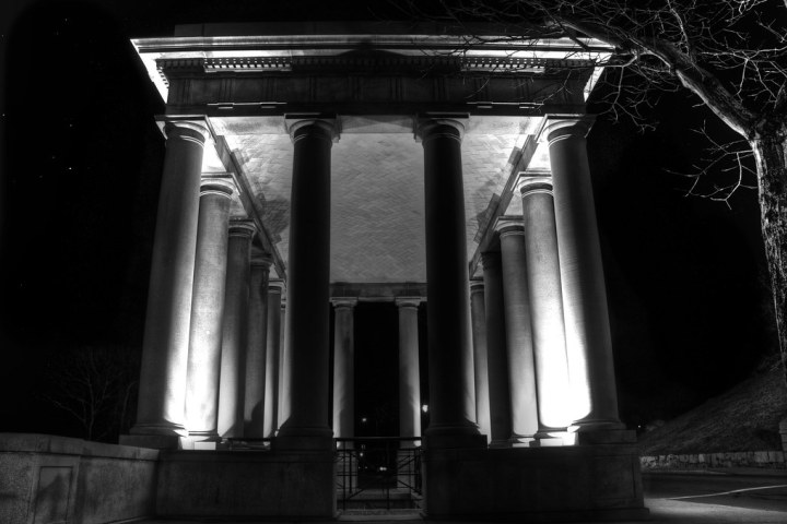 Illuminated columned structure at night with tree silhouette.