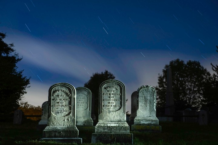 Gravestones in a cemetery under a night sky with star trails.