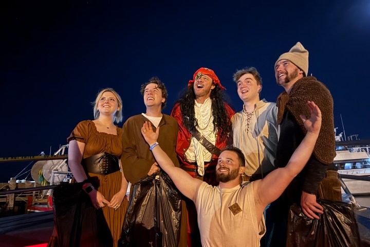 Six people in costume posing together under a dark sky on a ship deck.