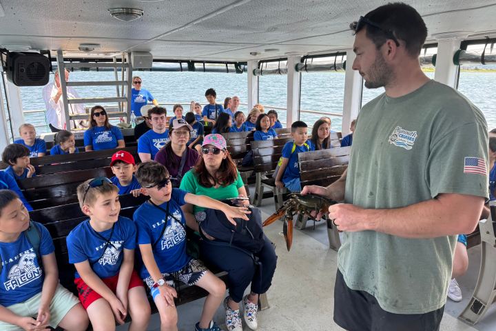 Instructor showing a large lobster to a group of seated children and adults on a boat.