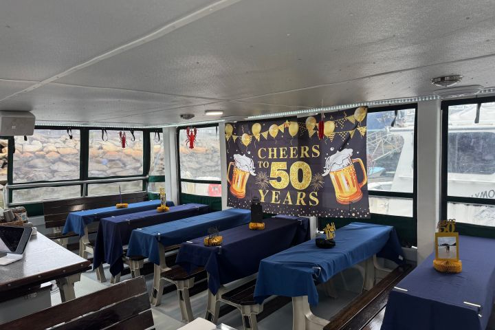Boat interior with tables set for a 50th celebration, banner reading 'Cheers to 50 Years' with beer mugs.