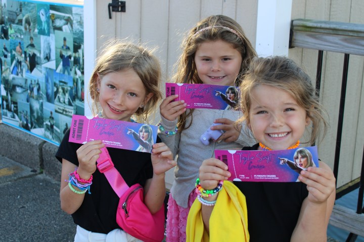 Three smiling girls holding concert tickets and wearing colorful bracelets.