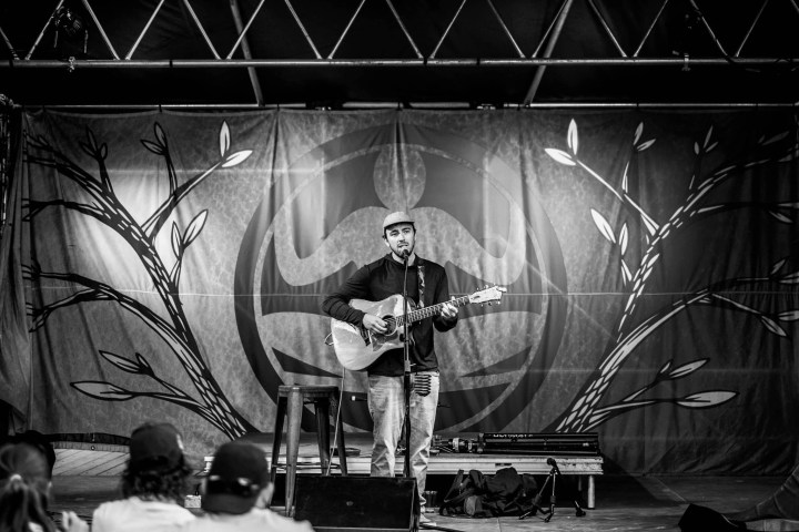 Singer with guitar performing on stage, floral backdrop, black and white photo.