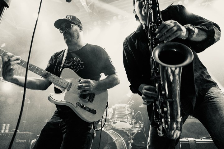 Black and white image of two musicians on stage, one with a guitar and the other with a saxophone.