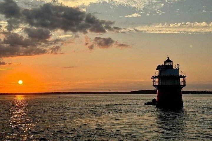 Sunset over water with a lighthouse silhouetted against the sky.