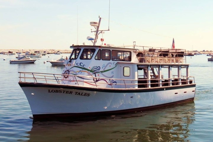 White boat named 'Lobster Tales' on calm water with other boats in the background.