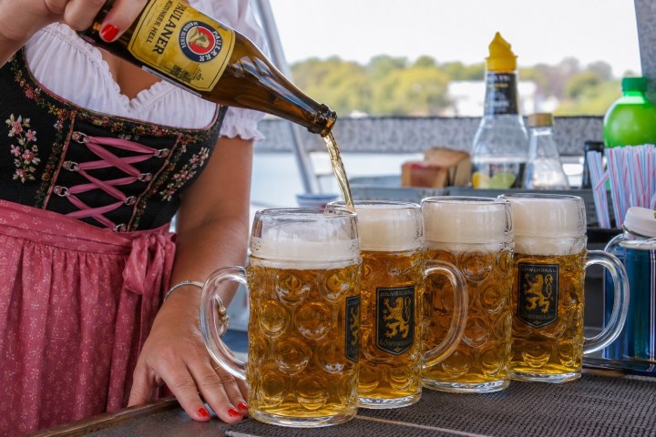 Person pouring beer into large mugs on a bar counter, outdoors.