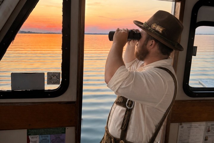 Man in traditional attire uses binoculars on a boat at sunset.